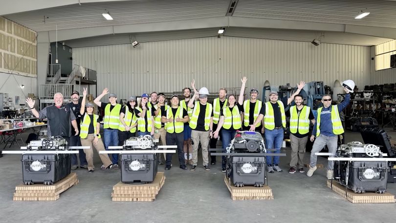 Outpost Space employees pose together outside in vests. 